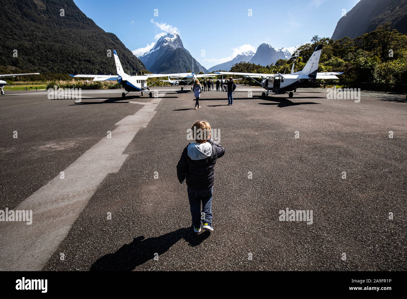 Little kid at airport runway with mountains in the back Stock Photo