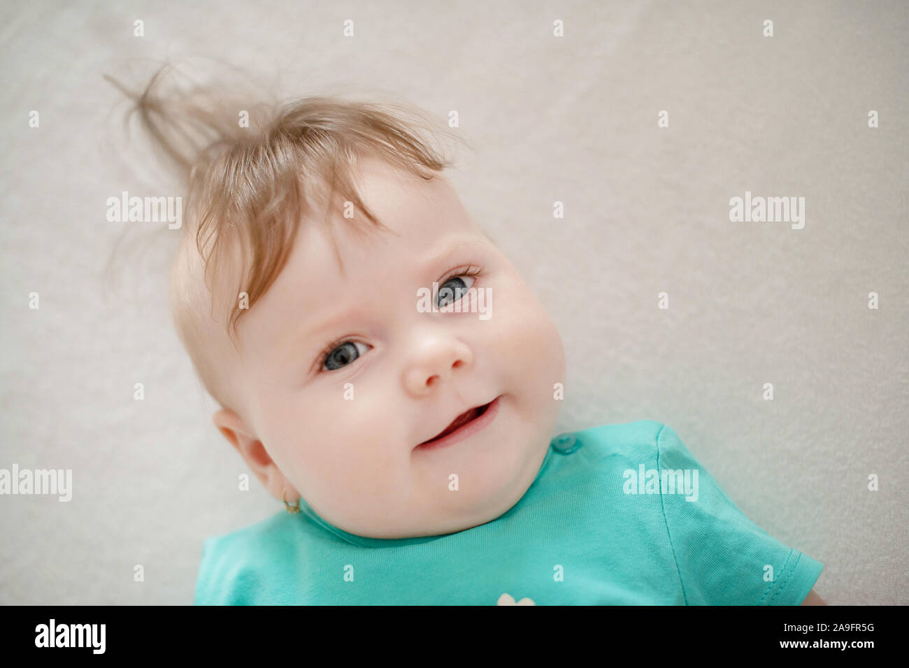 Portrait of adorable baby girl with blue eyes and cute hair looking at the camera calmly with a smile; cute baby facial expressions and learning steps Stock Photo