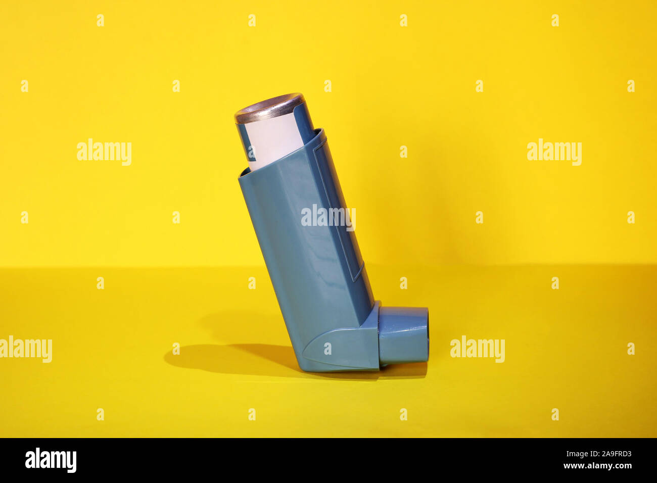 Blue asthma inhaler on a yellow background. Pharmaceutical product to prevent and treat an asthma attack. Stock Photo