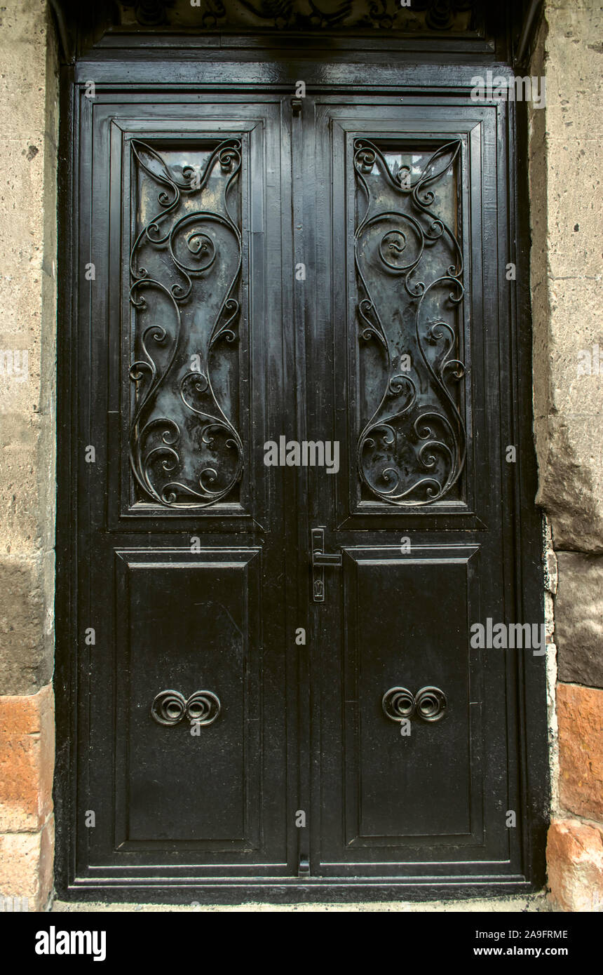 Black double leaf iron door covered with wrought iron decorative black bars on the facade of a stone building Stock Photo