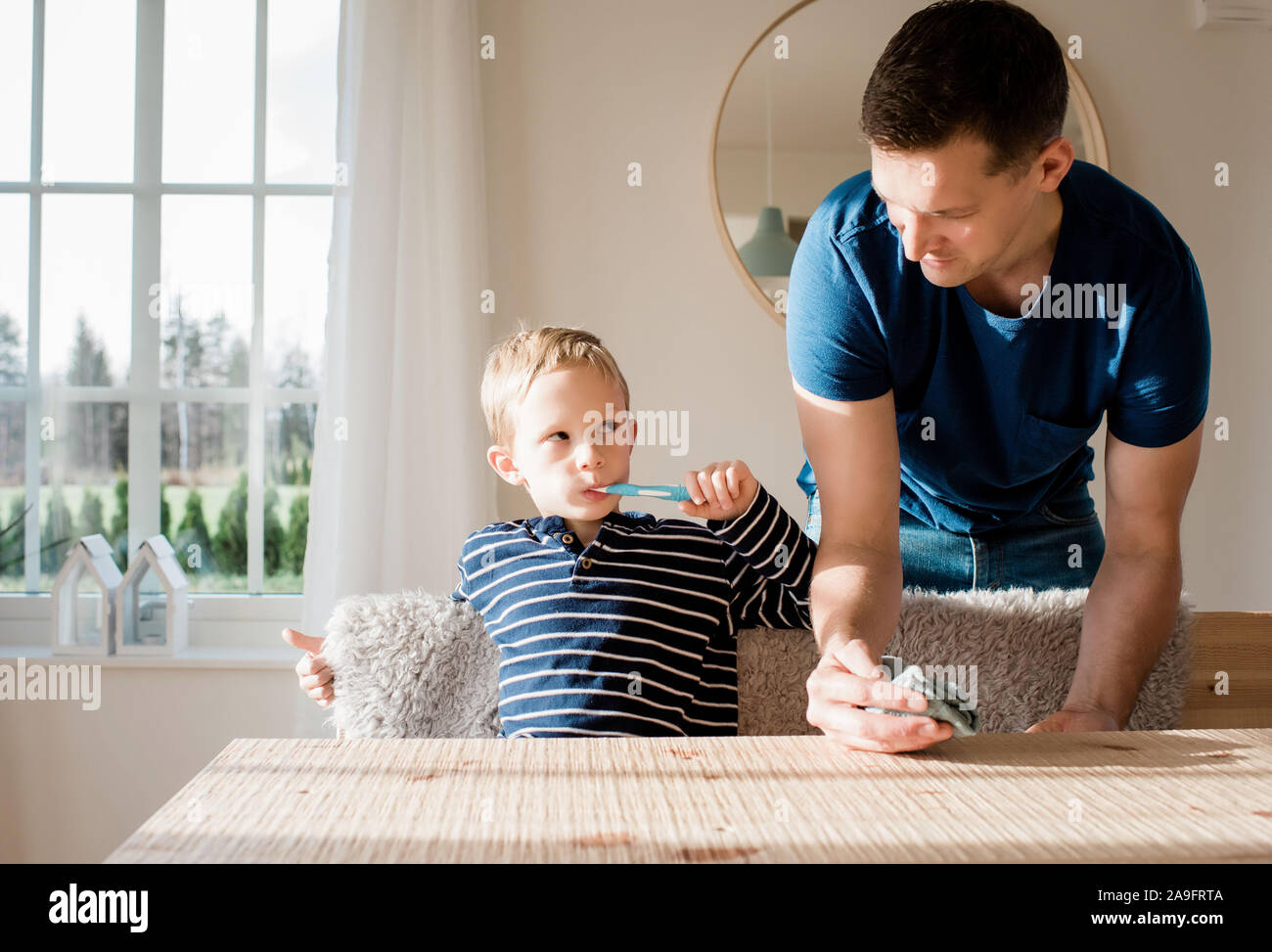 young boy brushing his teeth looking at his dad before school Stock Photo