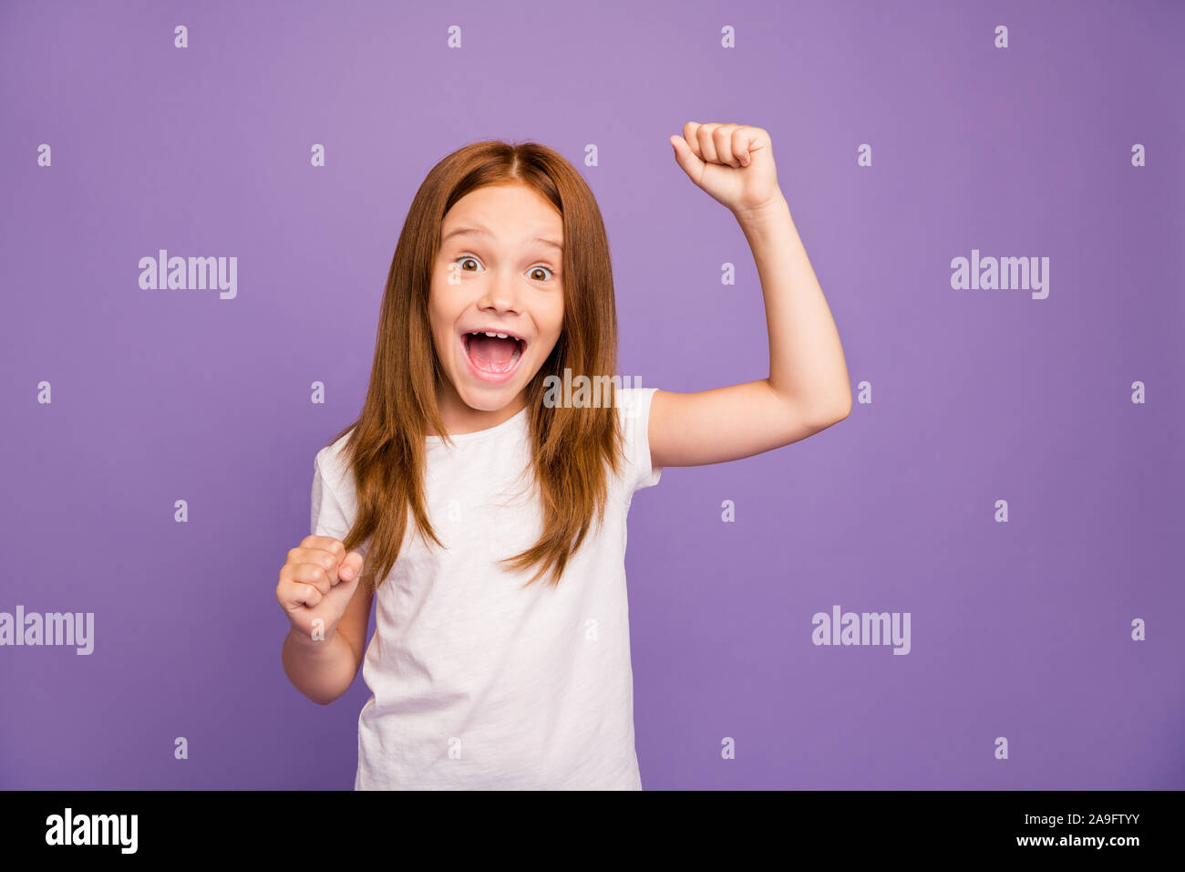 Photo of pretty excited little foxy lady raising fists screaming loudly got best examination grade results celebrating wear white t-shirt isolated Stock Photo
