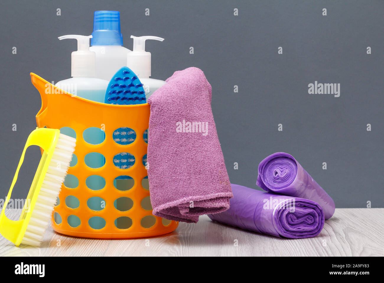 Plastic orange basket with bottles of dishwashing liquid, tile cleaner