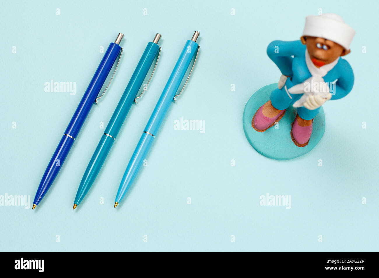 Three pens and plaster figure of a dentist on a blue background. Top view. Stock Photo