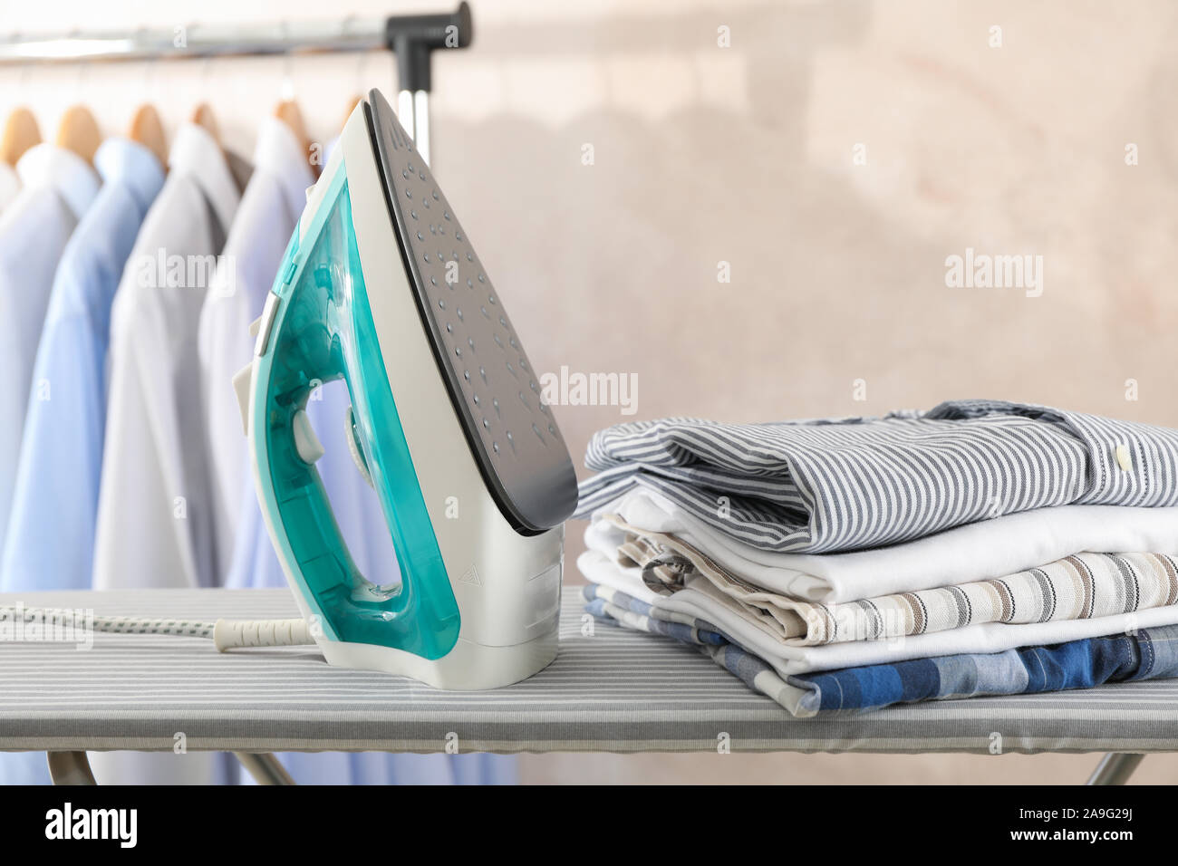 Iron and stack of t-shirts on ironing board, space for text Stock Photo