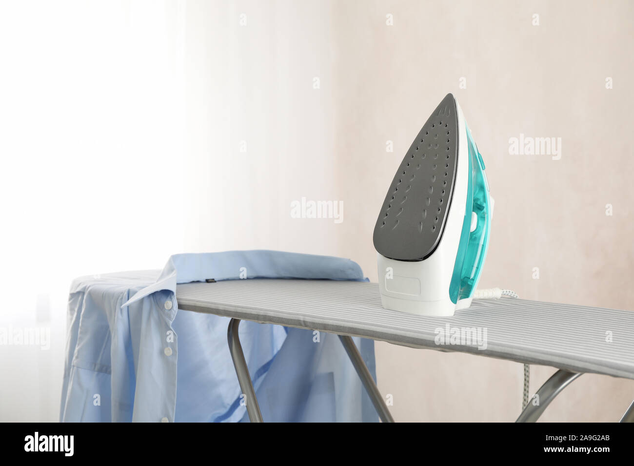 Iron and clean laundry on ironing board, space for text Stock Photo