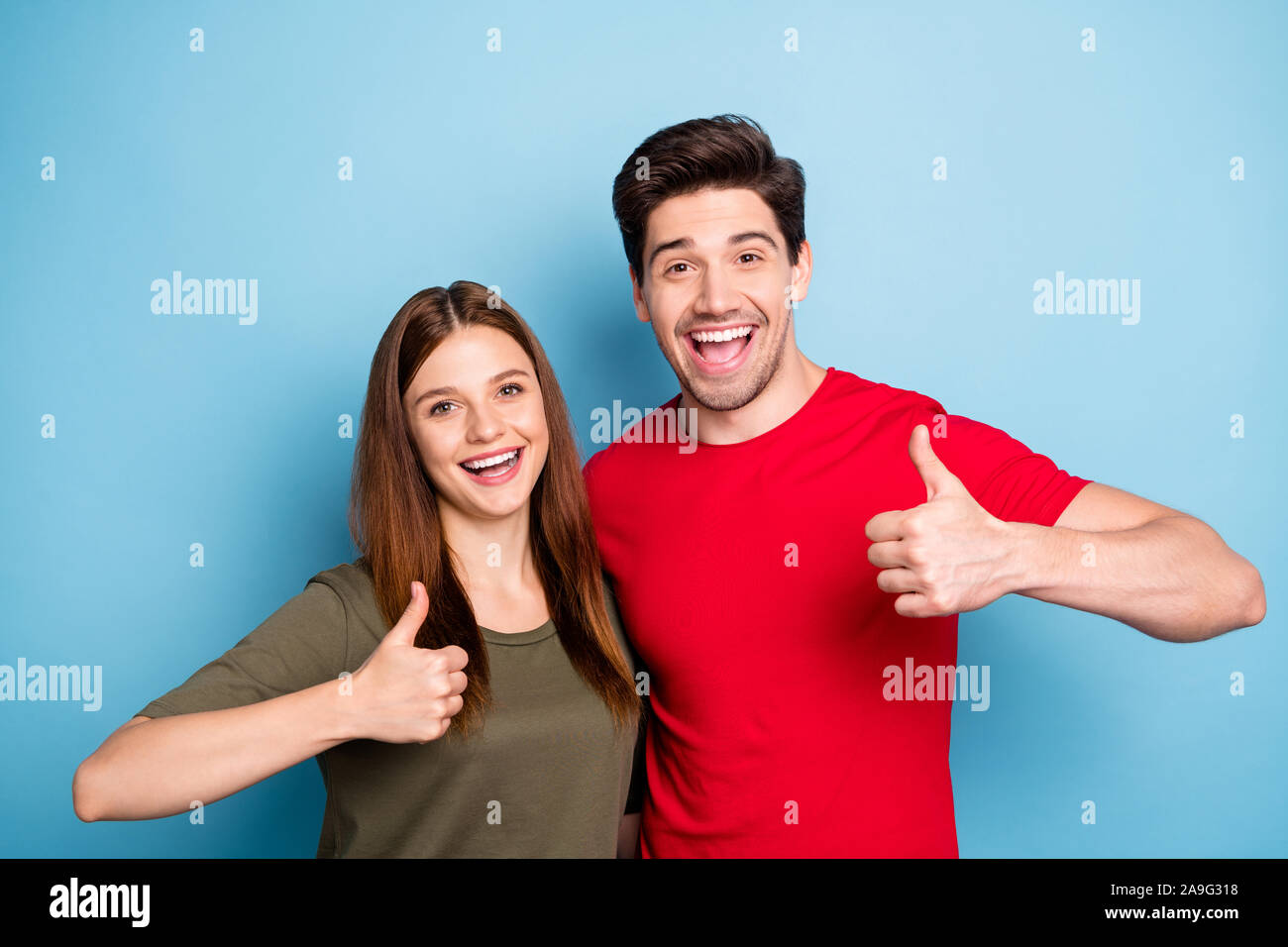 Portrait of romantic two spouses promoters show thumb up sign decide ads choose promo advice sales wear green red t-shirt isolated over blue color Stock Photo