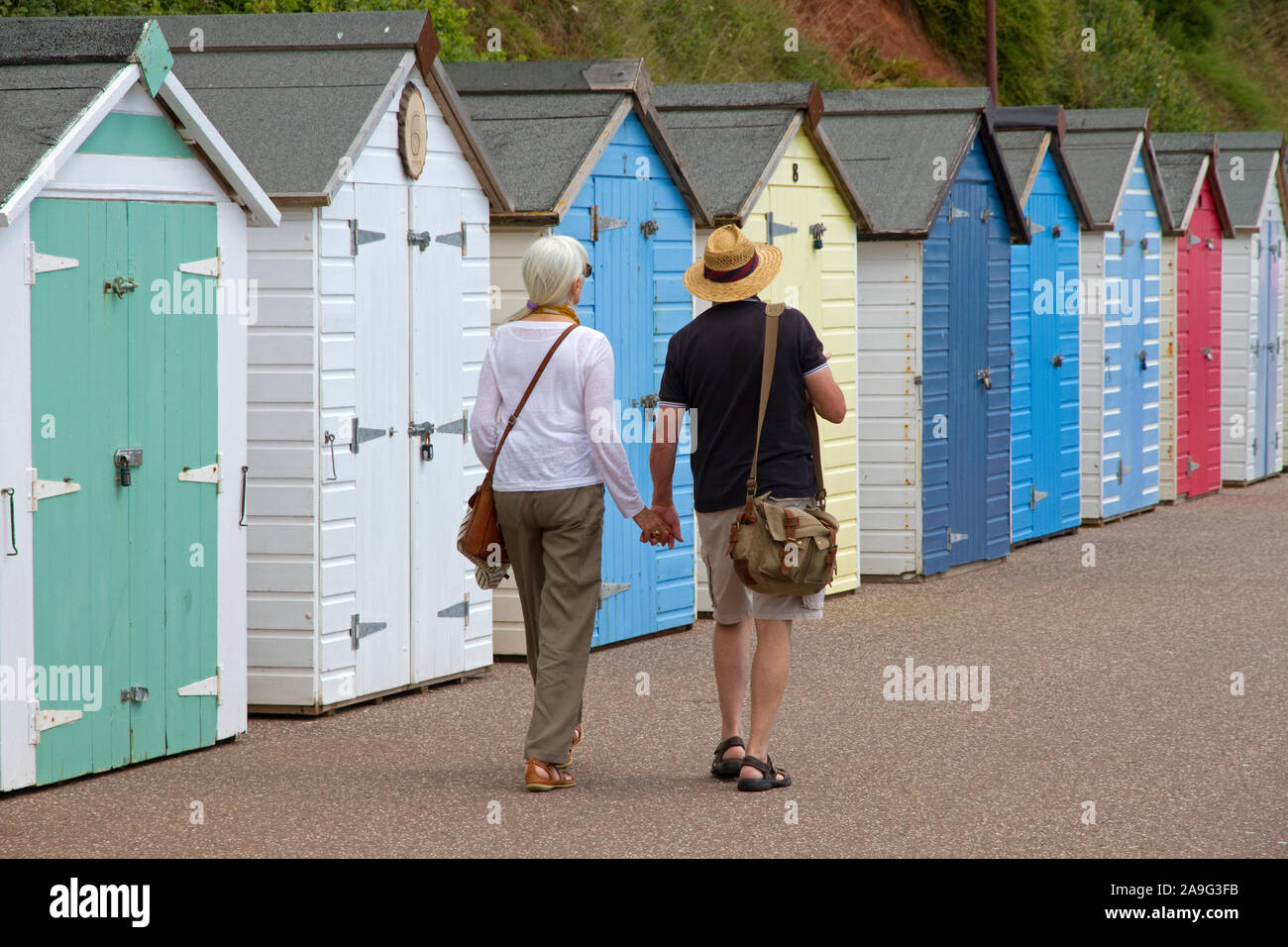 Couple walking past beach huts, promenade, Seaton, Devon, England, UK Stock Photo