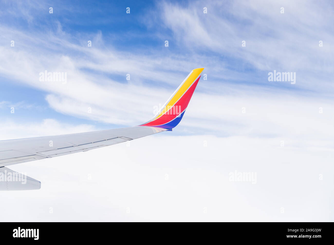 Looking out a Southwest airplane window in flight to see the wing, blue sky, and clouds. Stock Photo