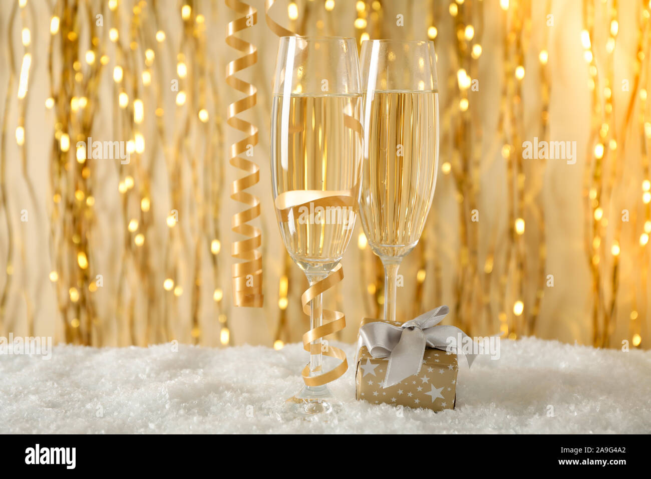 Champagne Glasses And Gift Against Background With Golden Ribbons