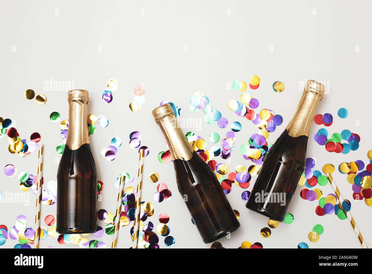 Composition with mini champagne bottles and glitter on white background, copy space Stock Photo