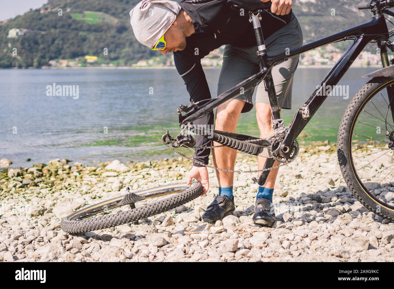 Bike Repair. Man Repairing Mountain Bike. Cyclist man in trouble rear wheel wheel case of accident. Man Fixes Bike near lake in Italy background Stock Photo