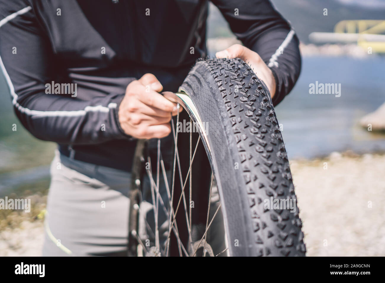 Bike Repair. Man Repairing Mountain Bike. Cyclist man in trouble rear wheel wheel case of accident. Man Fixes Bike near lake in Italy background Stock Photo