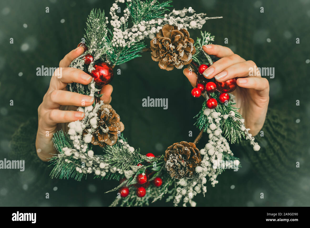 Pine wreath and Christmas decor in female hands on a green background. New Year Stock Photo