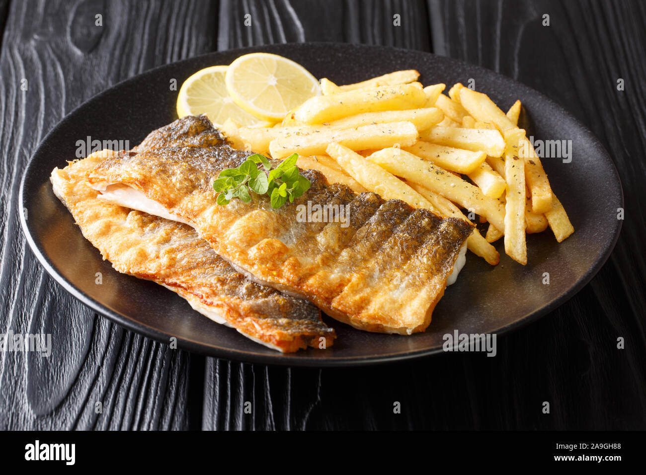 Tasty grilled sea bass fillet with french fries and lemon close-up on a plate on the table. horizontal Stock Photo