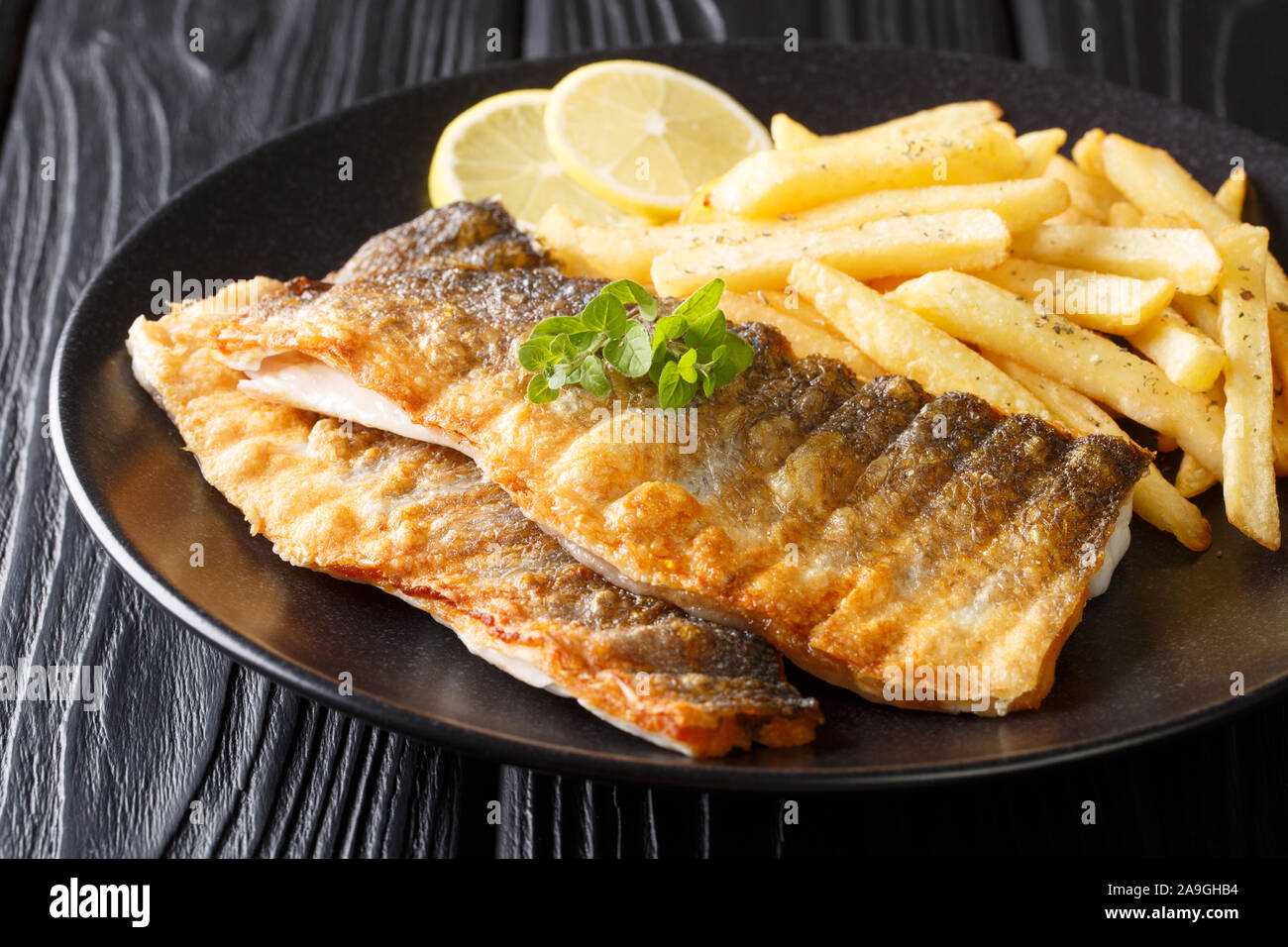 Spicy grilled sea bass fillet with crispy skin with french fries closeup on a plate on the