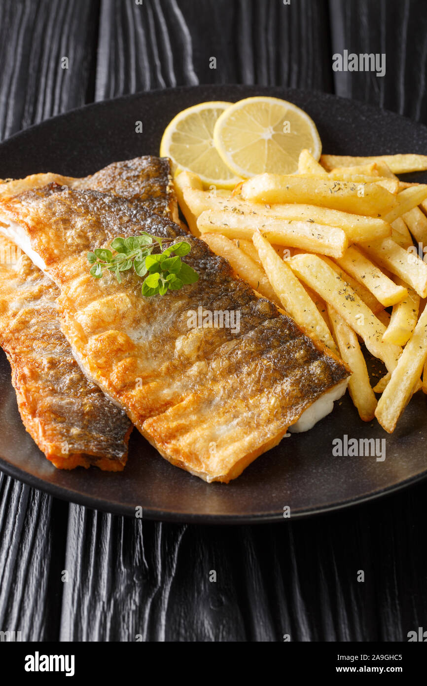 Delicious grilled sea bass filet served with french fries close-up on a plate on the table. vertical Stock Photo