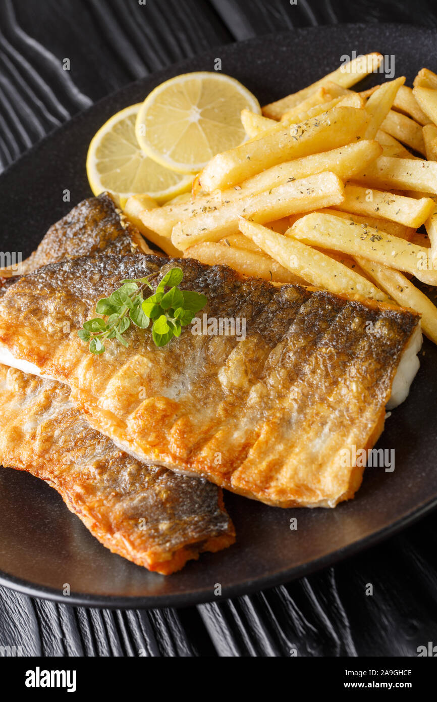Grilled sea bass fillet with french fries close-up on a plate on the table. vertical Stock Photo
