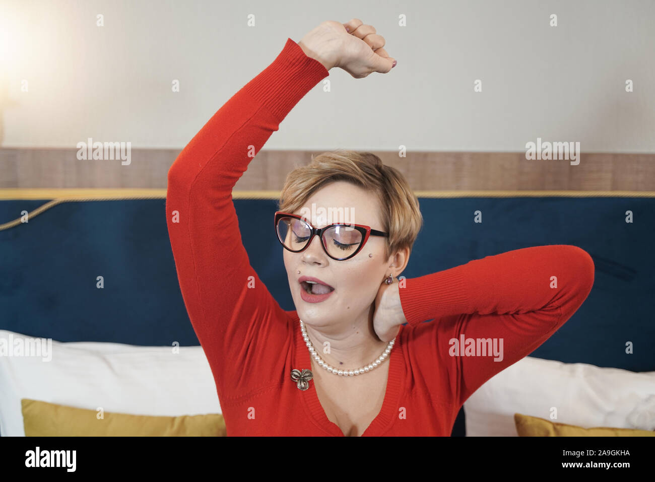 cute plus size short hair blonde girl in glasses yawns in the morning in  bed sitting in pajamas and stretching Stock Photo - Alamy