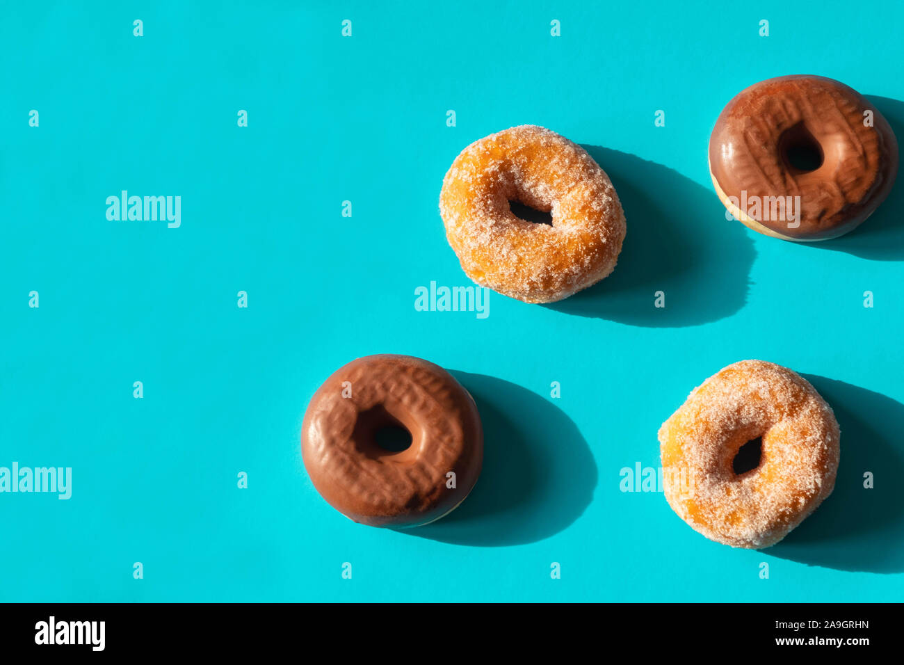 Chocolate frosted donuts and sugar coated donuts on bright blue paper background Stock Photo