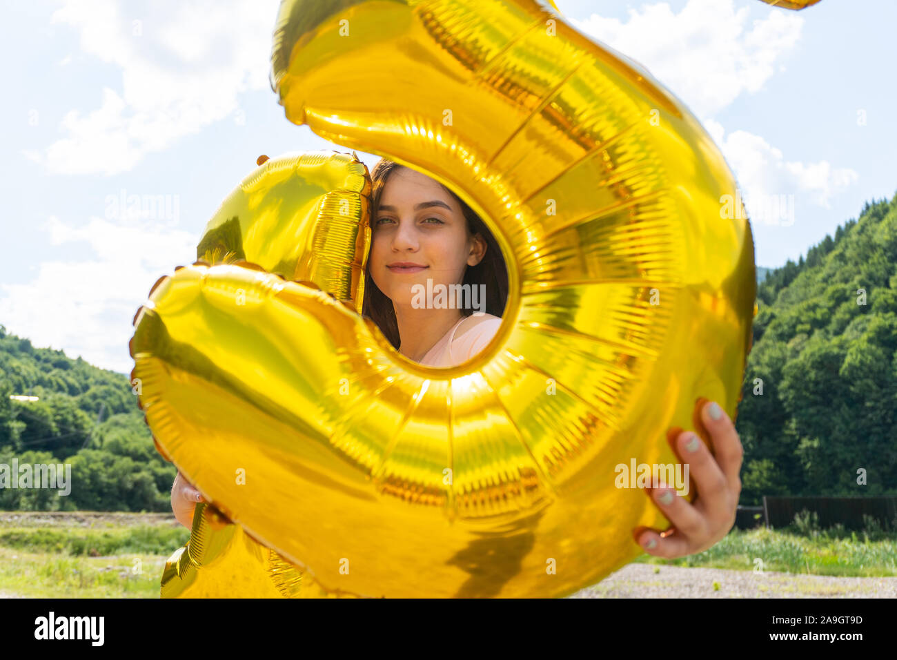 Teen girl looking through golden balloons in camera Stock Photo - Alamy