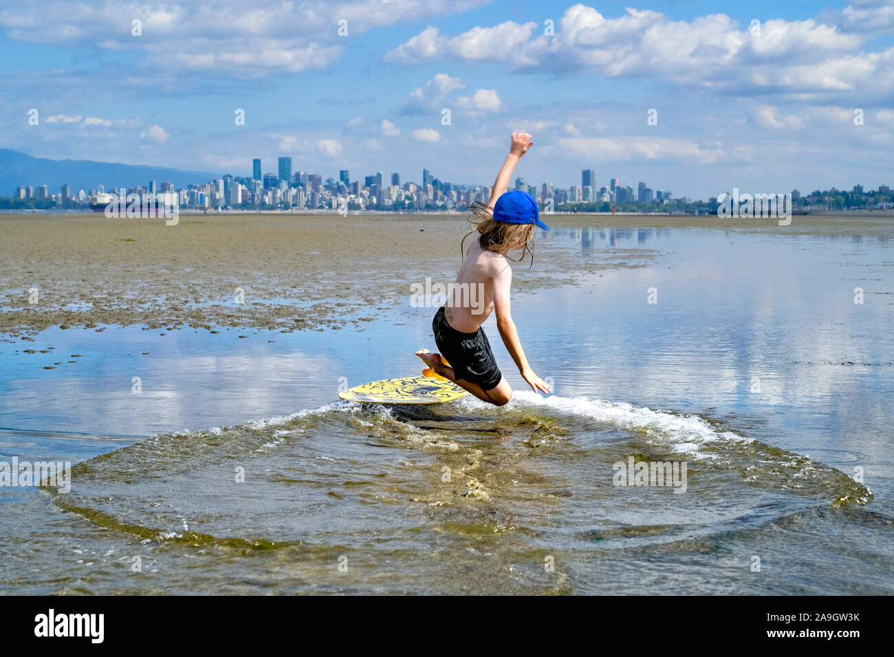 Young long haired boy skimboarding, Spanish Banks, English Bay, Vancouver, British Columbia, Canada Stock Photo