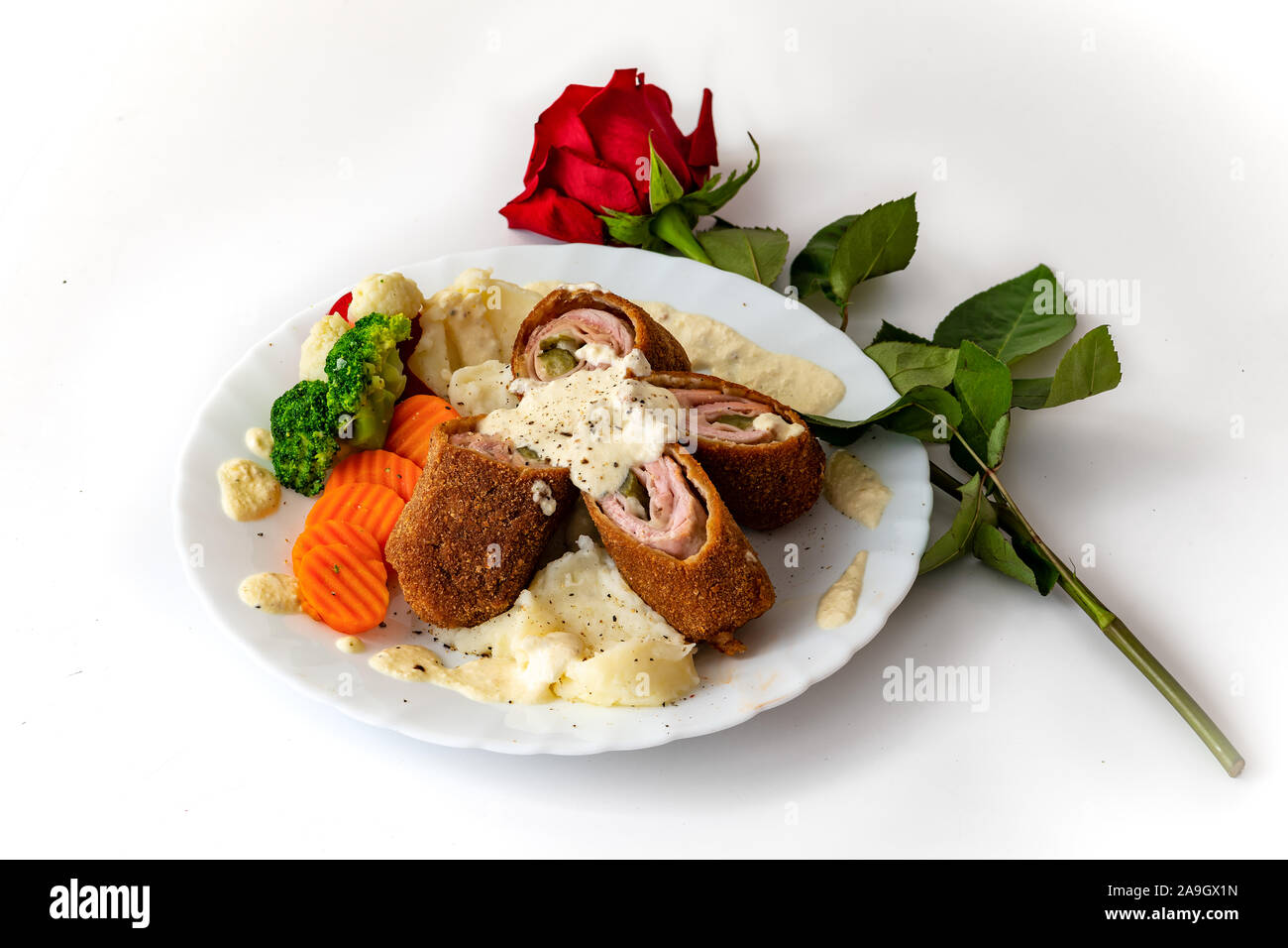 Karadjordjeva steak, it is a rolled veal or pork schnitzel,  with mashed pettitoes, boiled vegetables, Alfredo sauce  and a red rose as a decoration Stock Photo