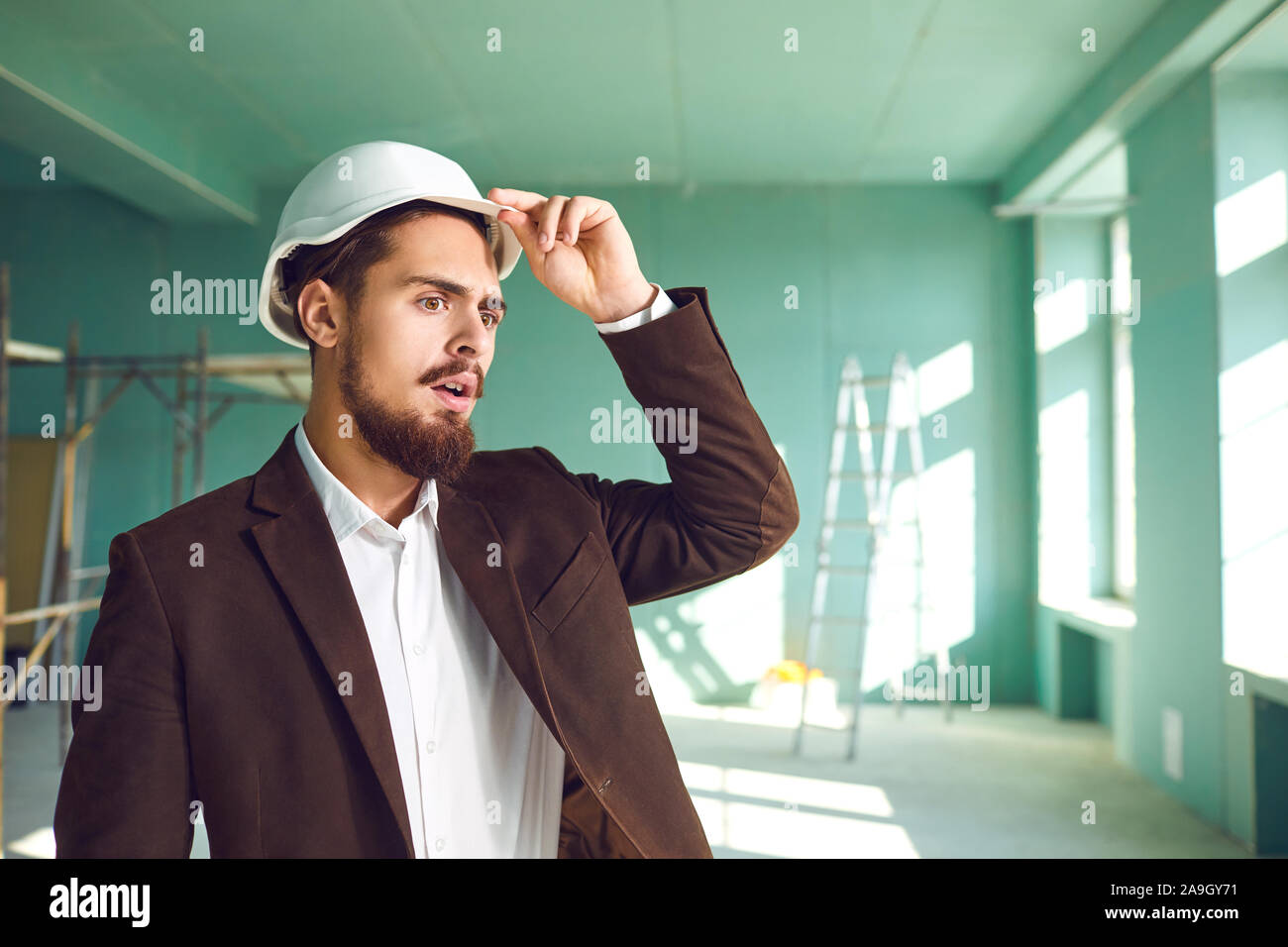 Builder foreman in a white helmet surprised in shock at a construction site indoors Stock Photo