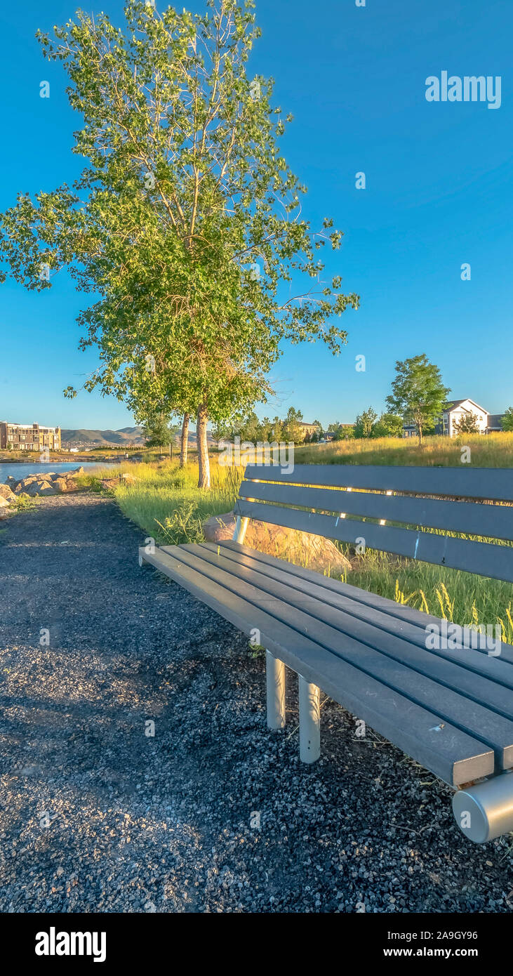 Vertical Bench at the shore of a lake with homes and buildings background on a sunny day Stock Photo