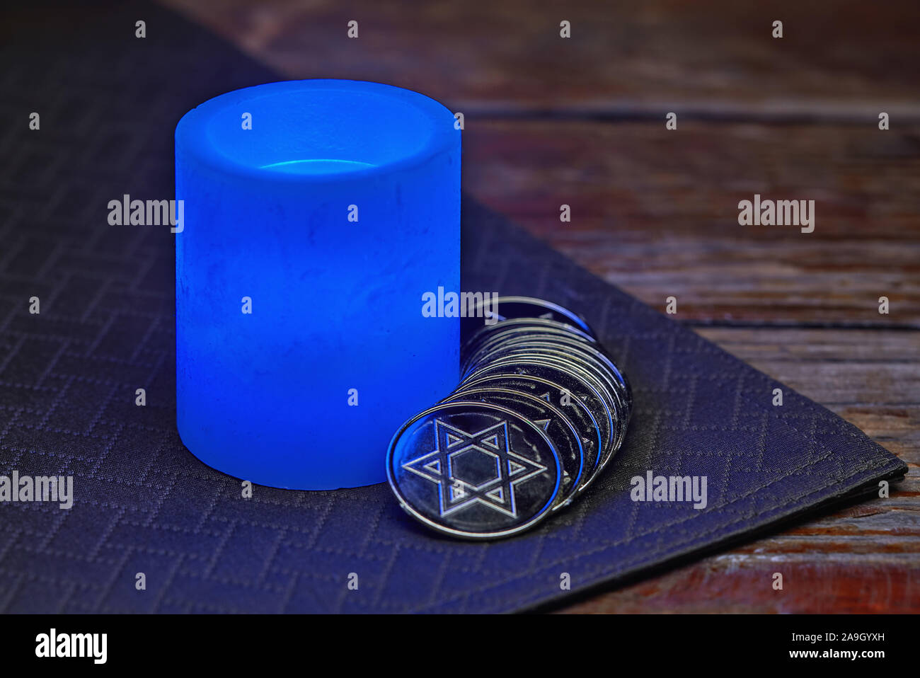 Hanukkah still life of glowing blue electric candle and gold coins Stock Photo