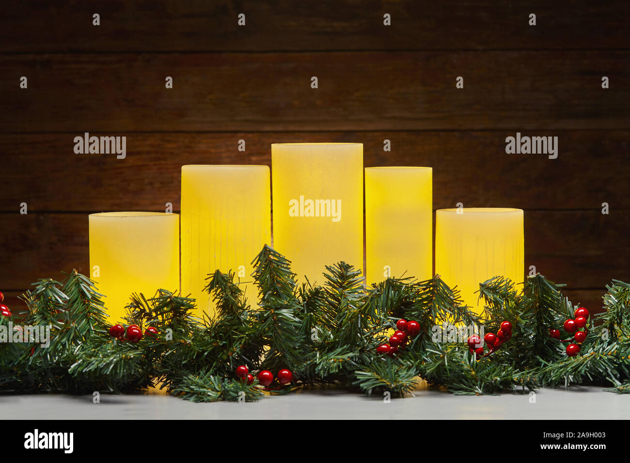 Christmas holiday still life of glowing yellow electric candles and green garland with holly berries Stock Photo