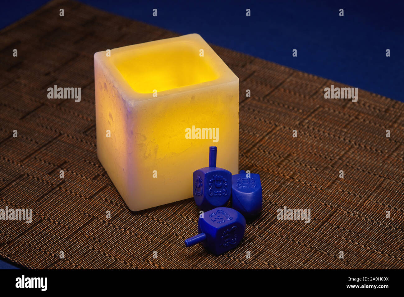 Hanukkah still life of glowing yellow electric candle and blue dreidels Stock Photo