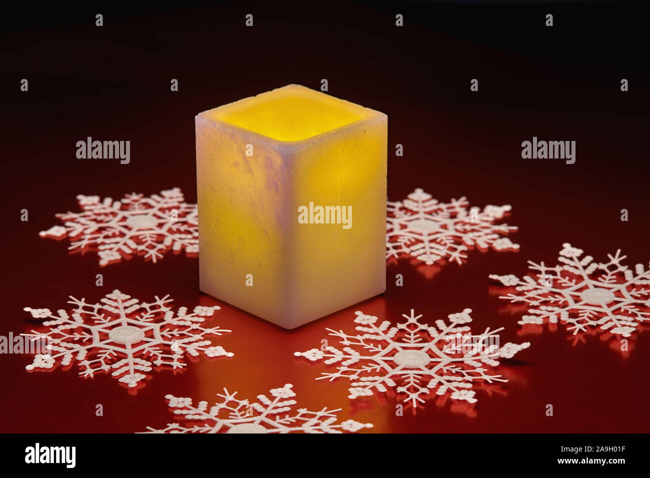 Winter holiday still life of glowing square electric candle and white snowflakes on red tabletop Stock Photo