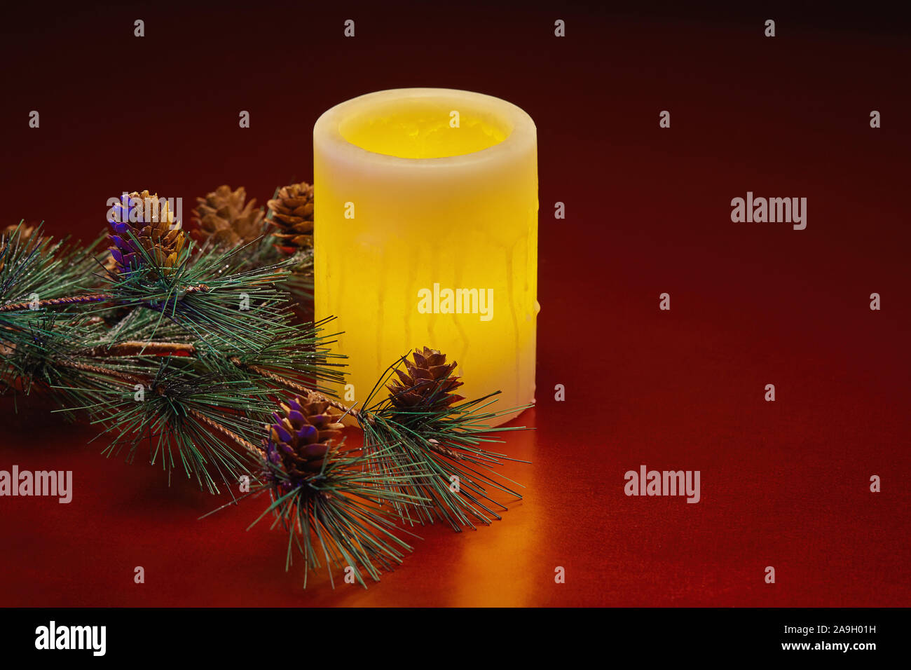 Winter holiday still life of glowing electric candle and a pine tree branch with pine cones Stock Photo