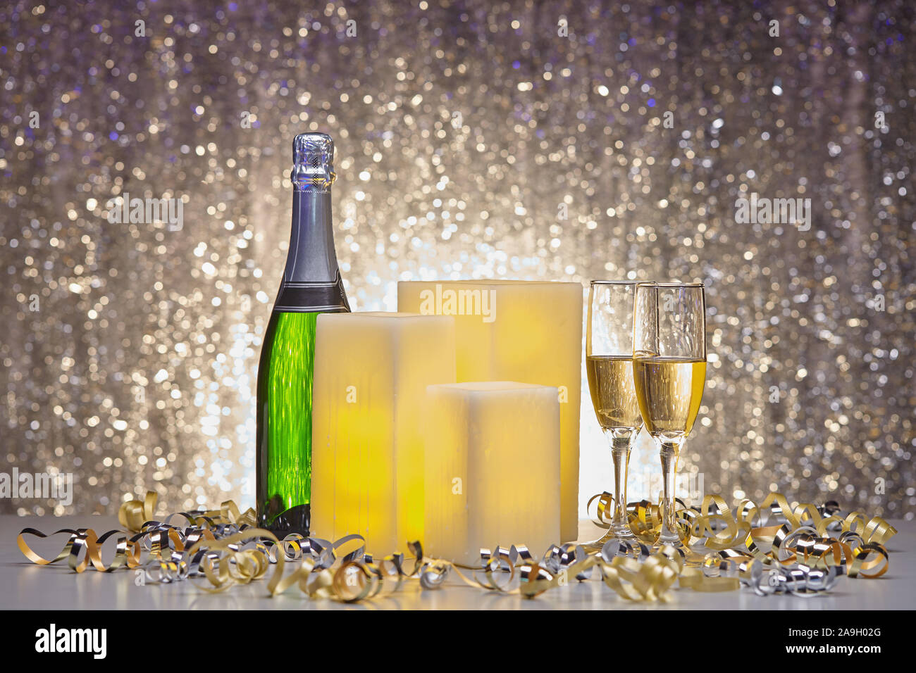 New years eve still life of electric wax candles, flutes of champagne and silver and gold party ribbon Stock Photo