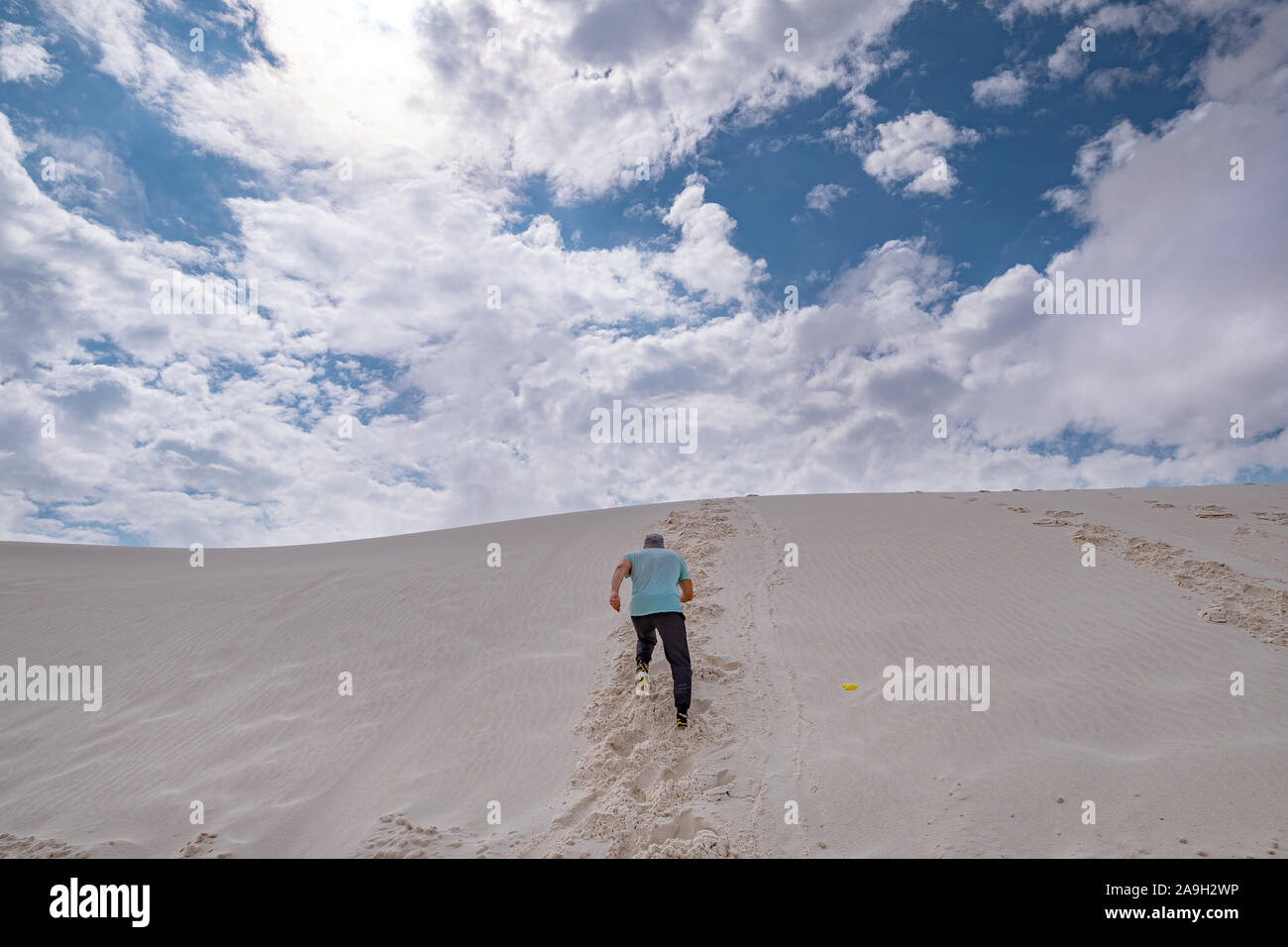 man in casual clothing running up a white sand dune against blue sky Stock Photo