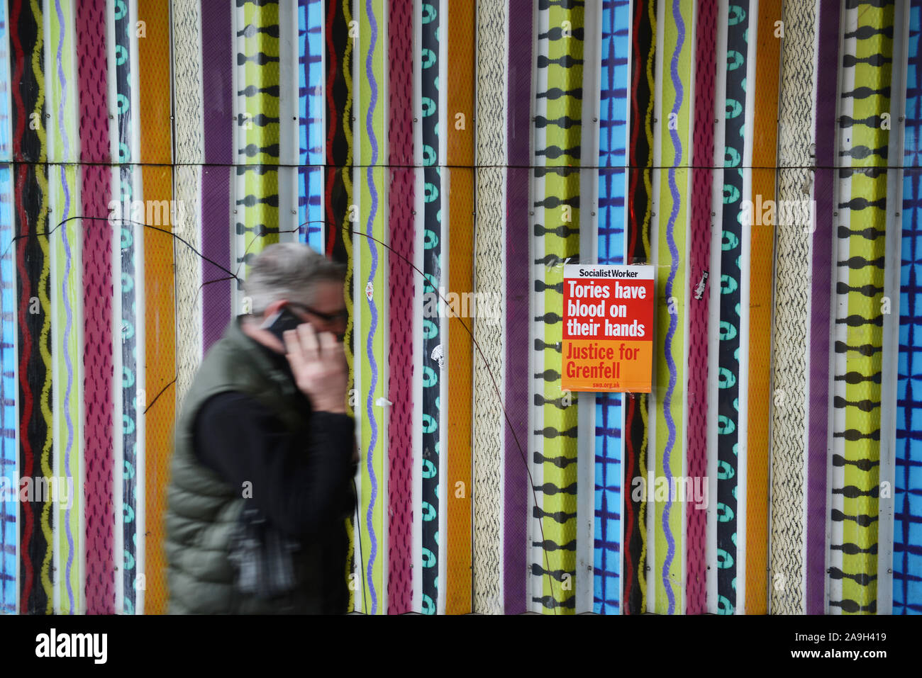 A man on his mobile phone walks past a Socialist Worker poster near Ladbroke Grove tube station in Notting Hill, London.  The poster reads: 'Tories have blood on their hands Justice for Grenfell'. Stock Photo