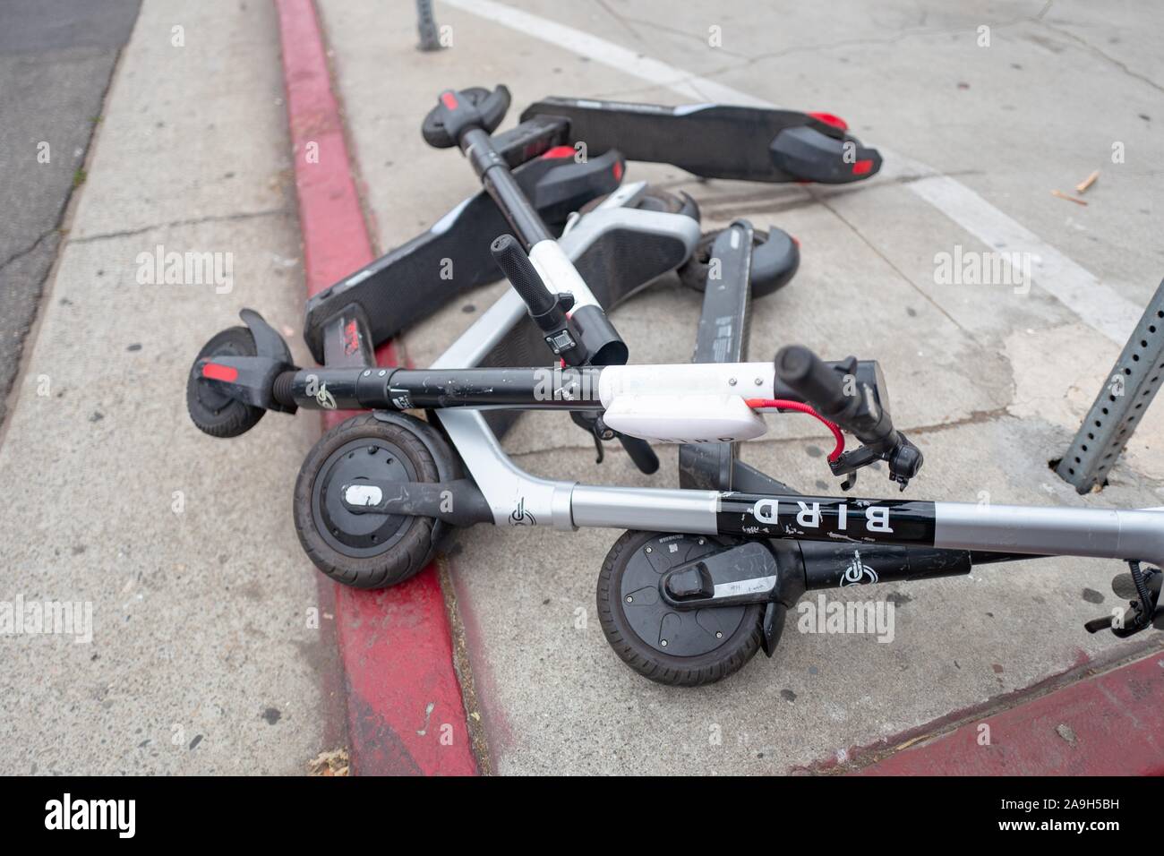 Close-up of a pile of fallen micromobility electric scooters from various companies on a sidewalk in Los Angeles, California; a criticism of the scooter's has been their tendency to be discarded by users in inconvenient locations, where they risk blocking sidewalks and roads, October 27, 2019. () Stock Photo