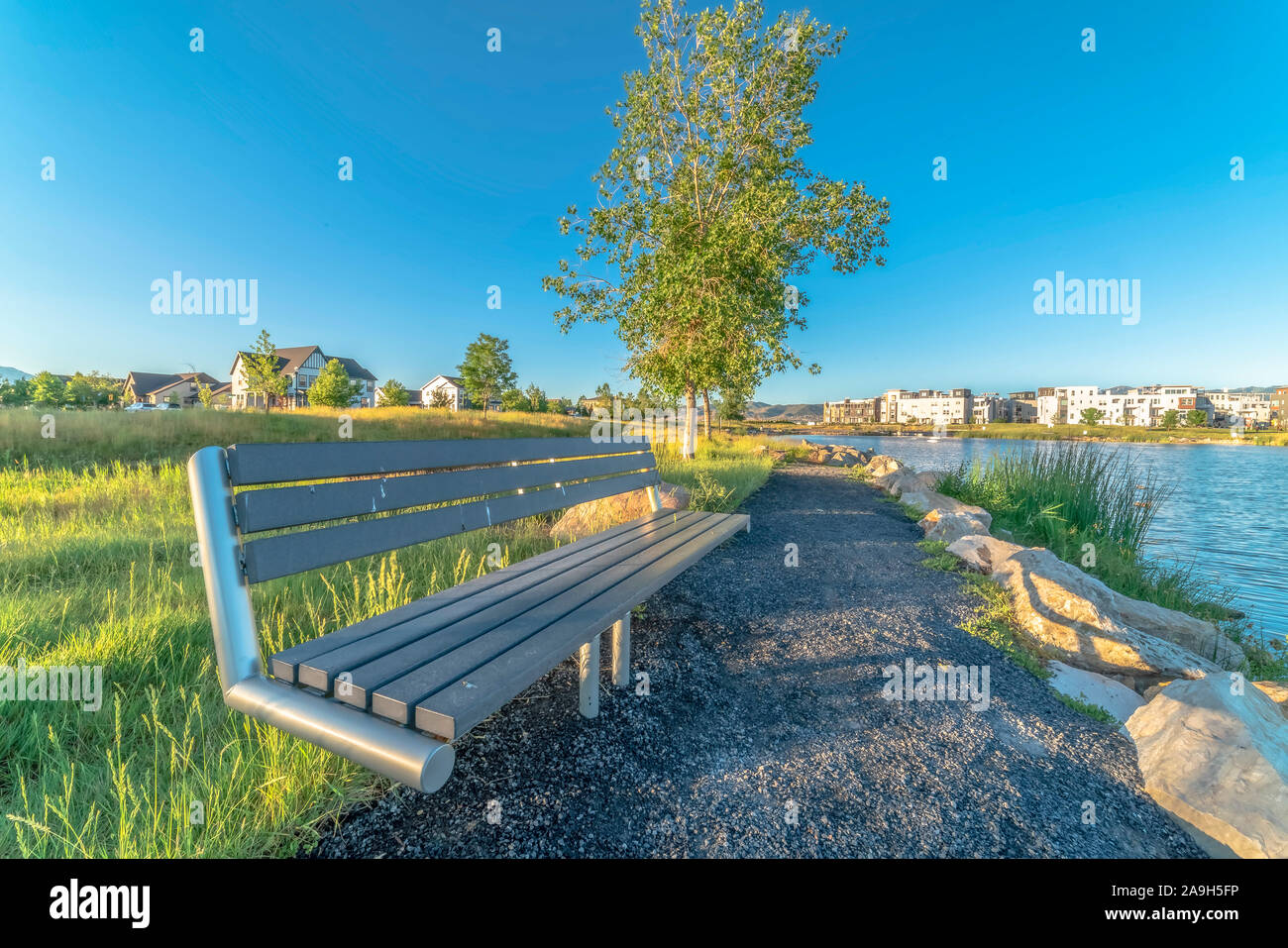 Bench at the shore of a lake with homes and buildings background on a sunny day Stock Photo