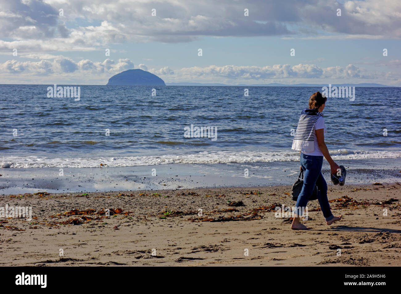 Woman walking on the beach at Girvan in South Ayrshire, Scotland with Ailsa Craig in the distance. Stock Photo