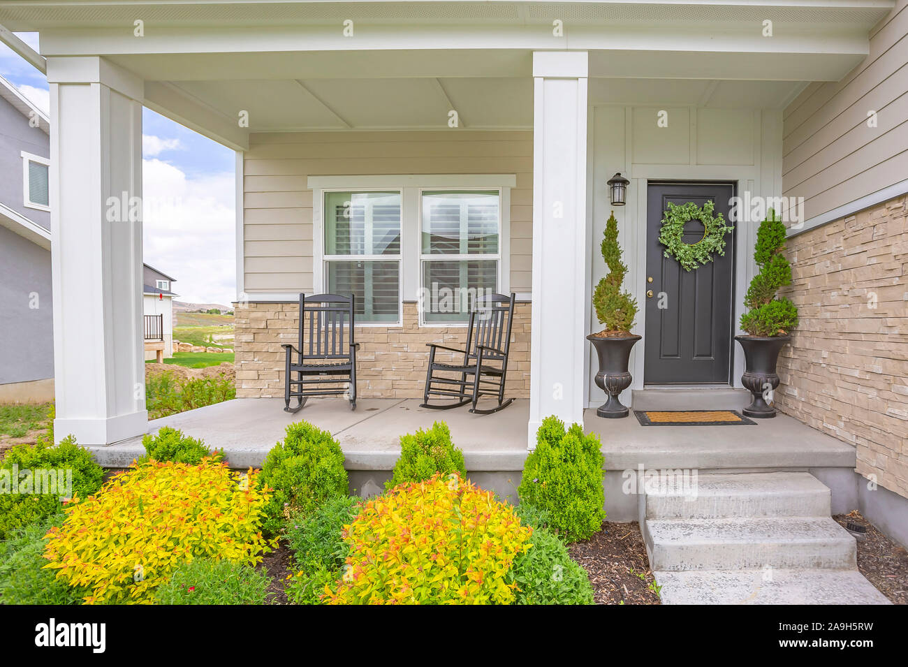 Home facade with stairs leading to porch with pillars and gray door with  wreath Stock Photo - Alamy