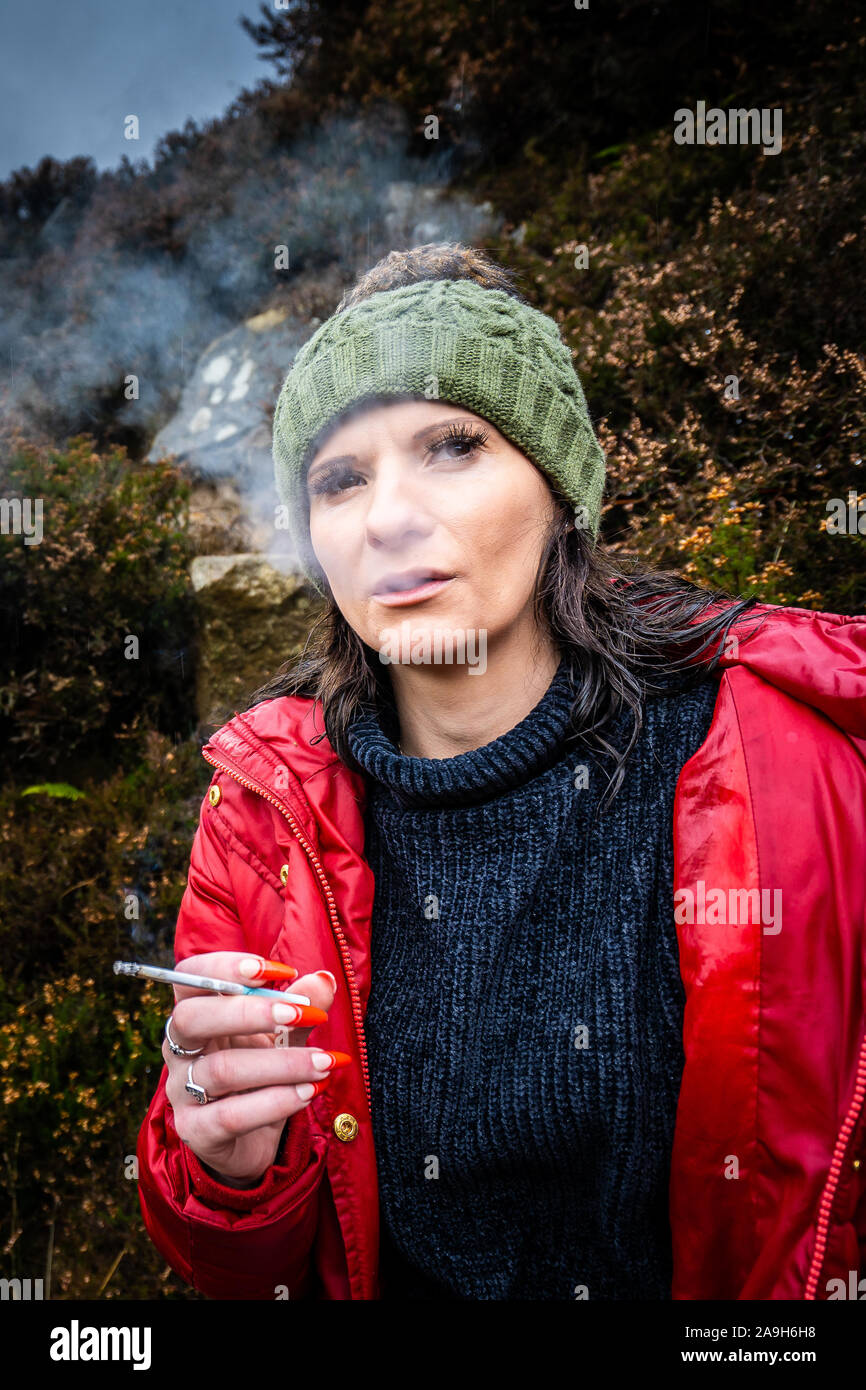A young women wearing a warm hat and red coat takes a break from hiking mountain climbing to have a smoke cigarette break and get some rest Stock Photo Alamy