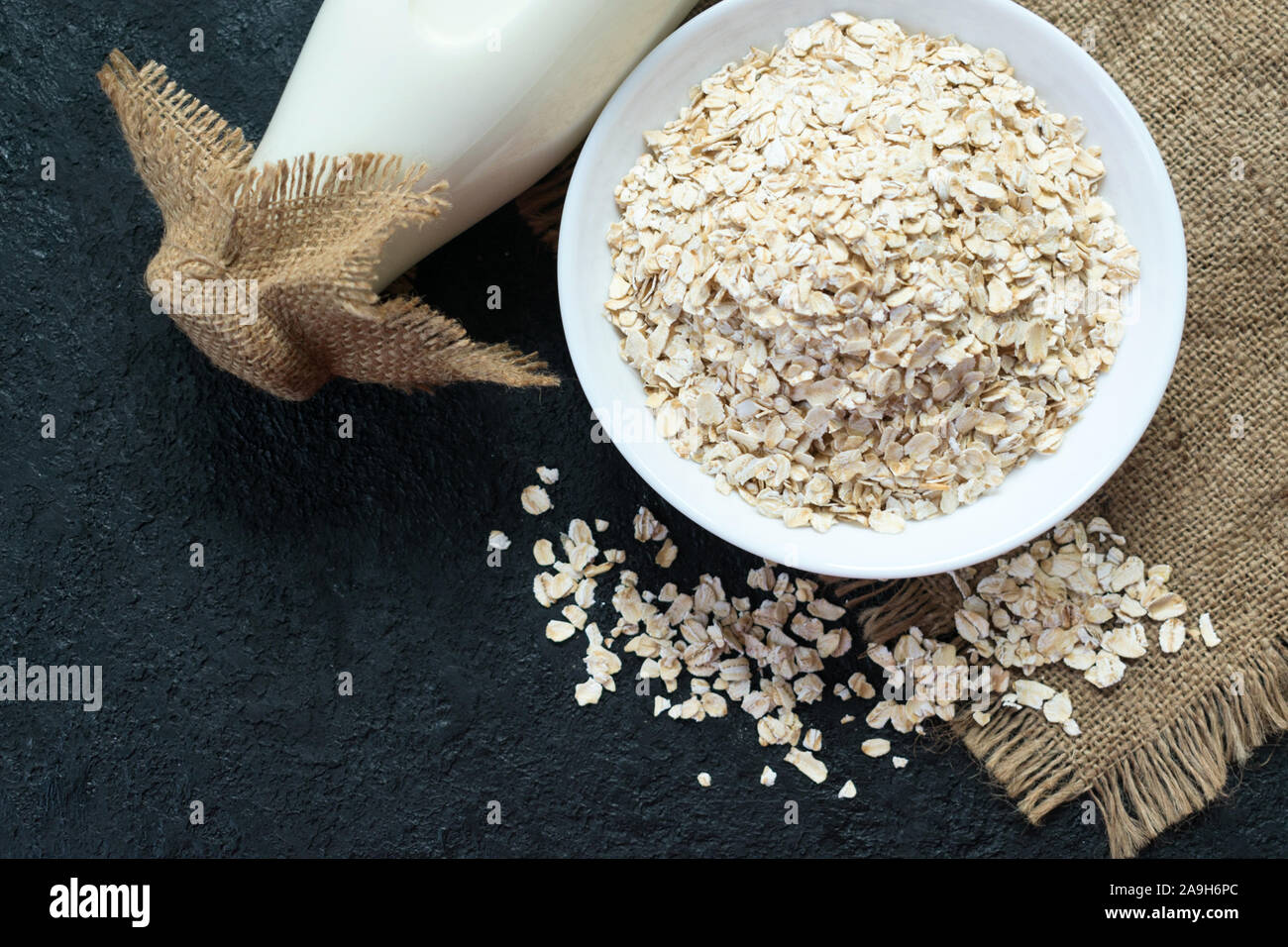 A bottle of oat milk and a plate of oatmeal on a black background. The concept of vegetarian food. Stock Photo