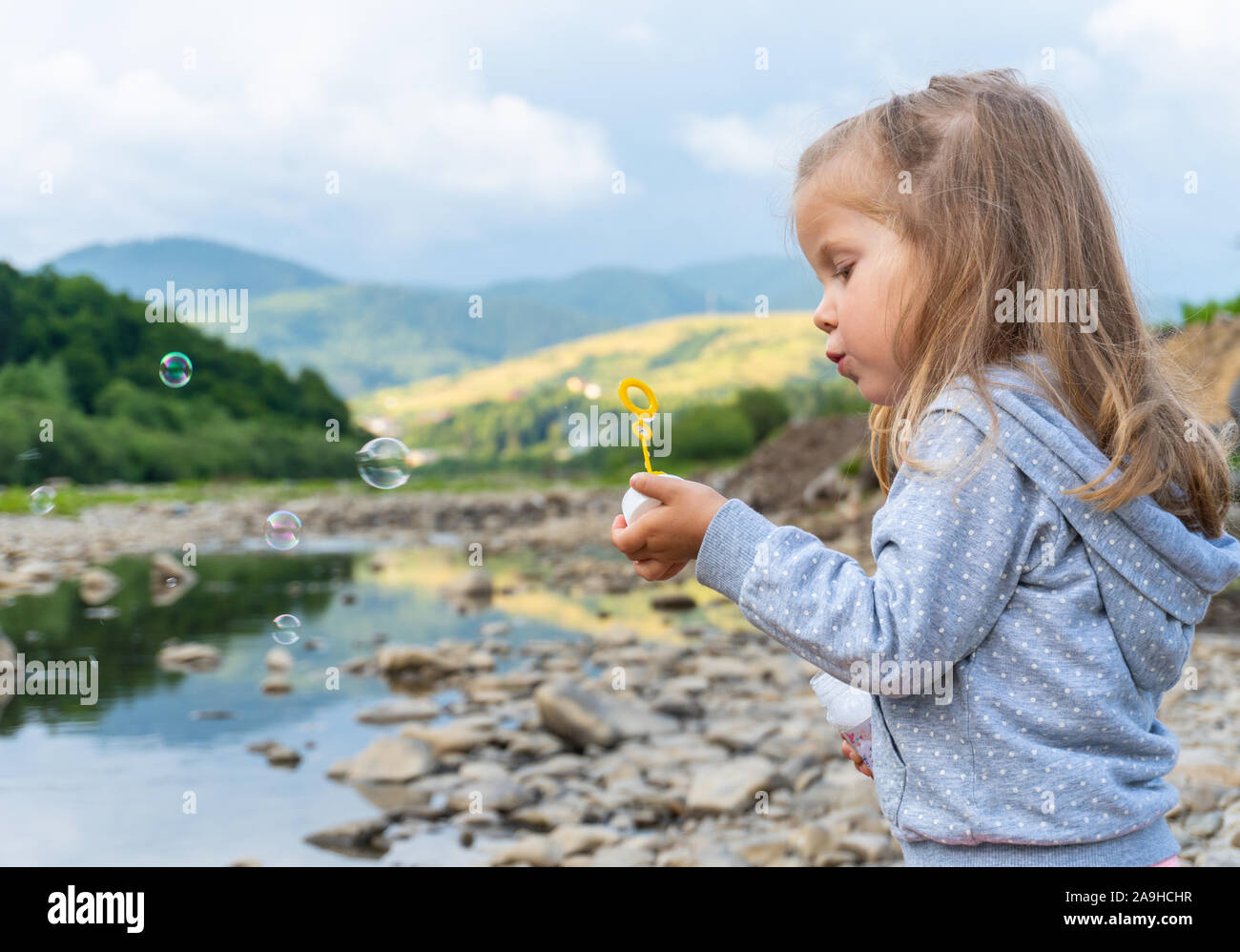 Little girl playing with soap bubbles near mountain river Stock Photo