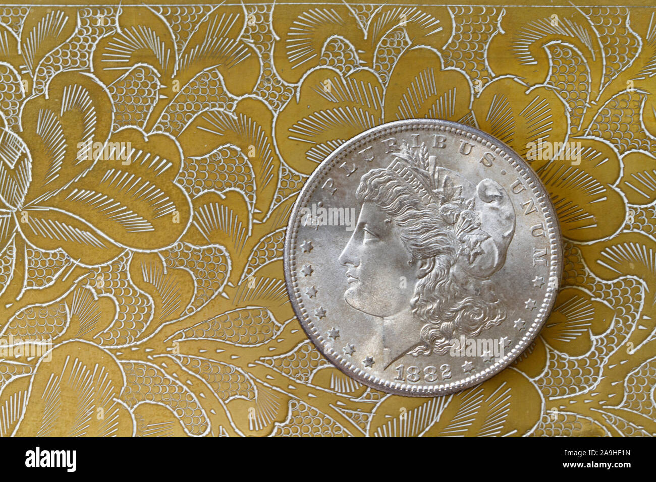 Uncirculated Morgan Silver Dollar against Gold tones of a Brass Background Stock Photo