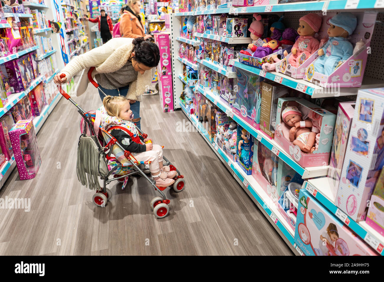 A cute little girl of toddler age in her buggy with her mother looking at gifts in a toy shop for Christmas, browsing and Christmas shopping, Xmas Stock Photo