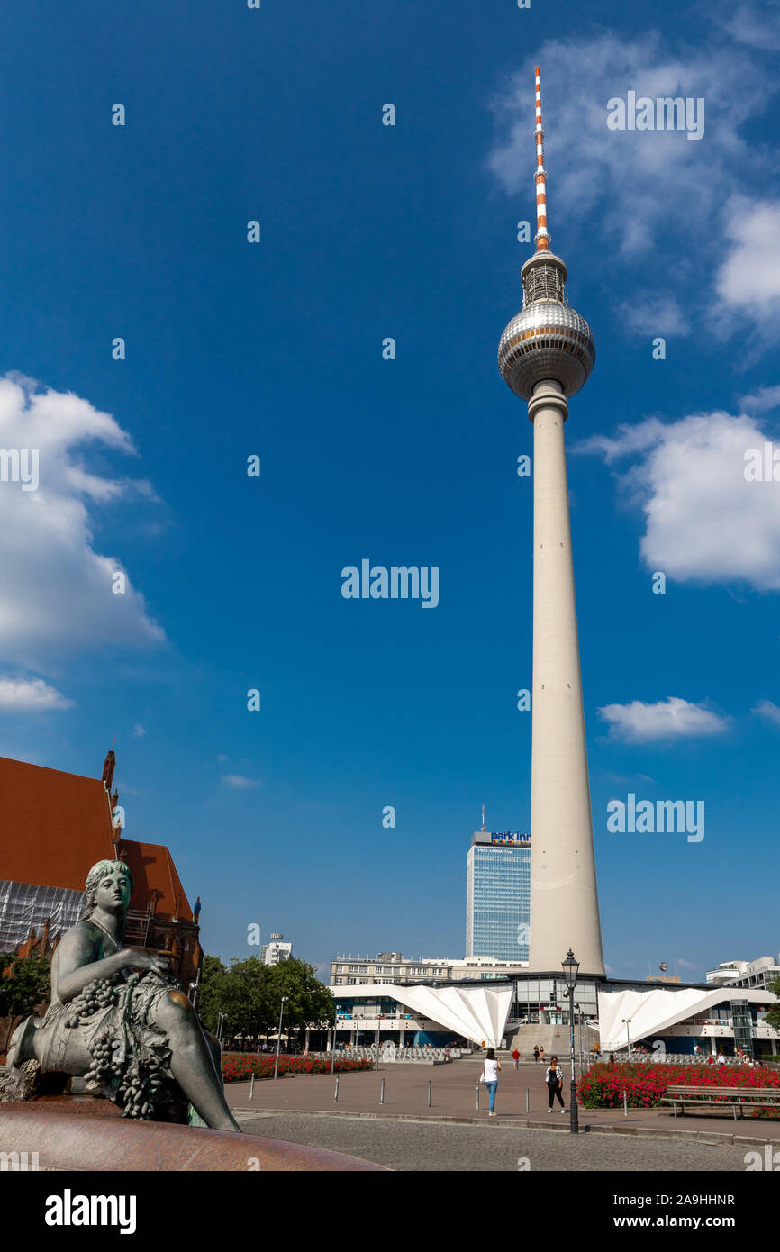 Berlin Germany - June 2019: Bottom View Of Berliner Fernsehturm (TV Tower) Under Blue Sky With Lady Sculpture In Foreground. Stock Photo