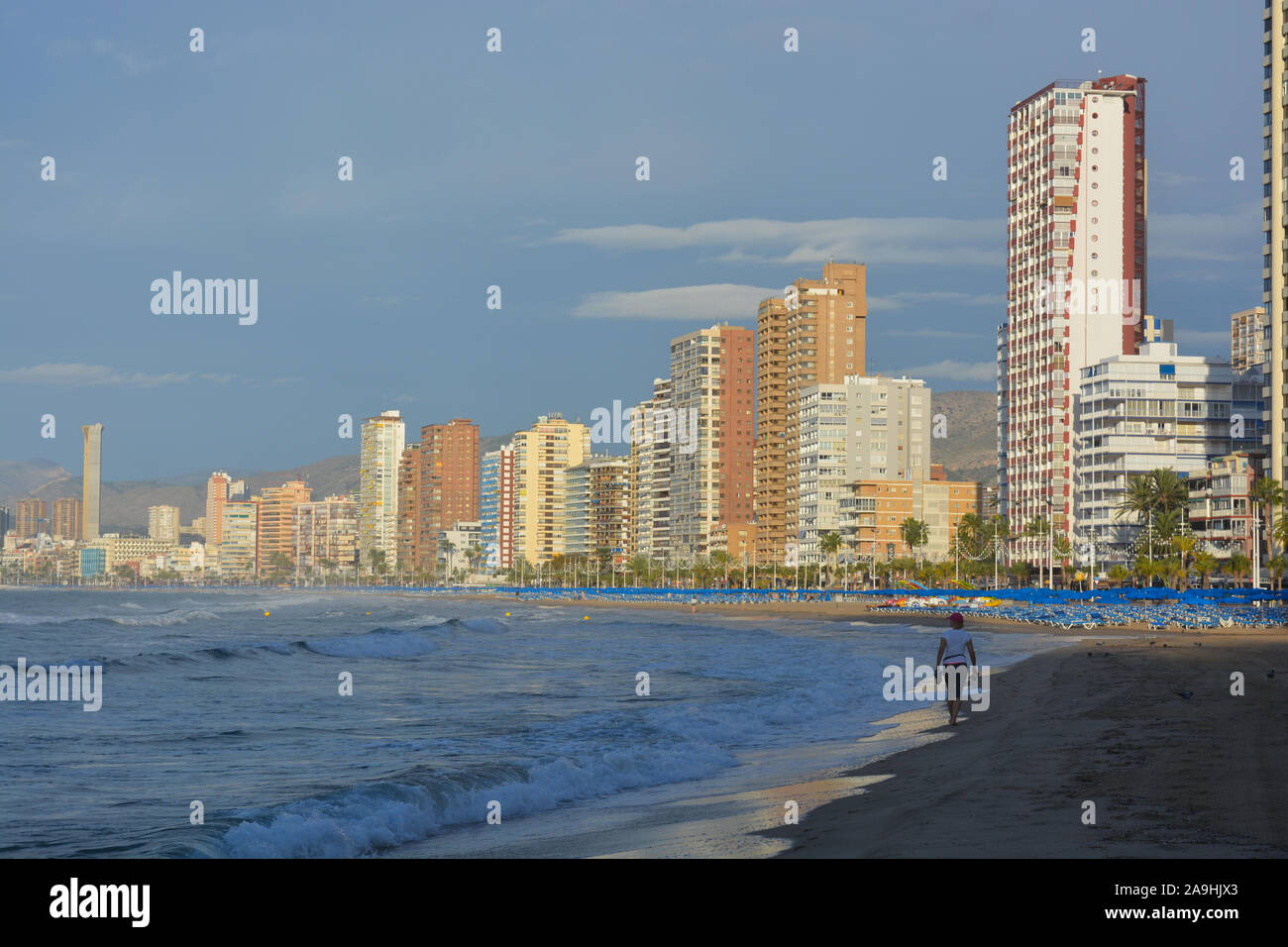 Benidorm city skyline and Playa Levante beach, early morning with woman walking on the beach and reflections in wet sand Stock Photo