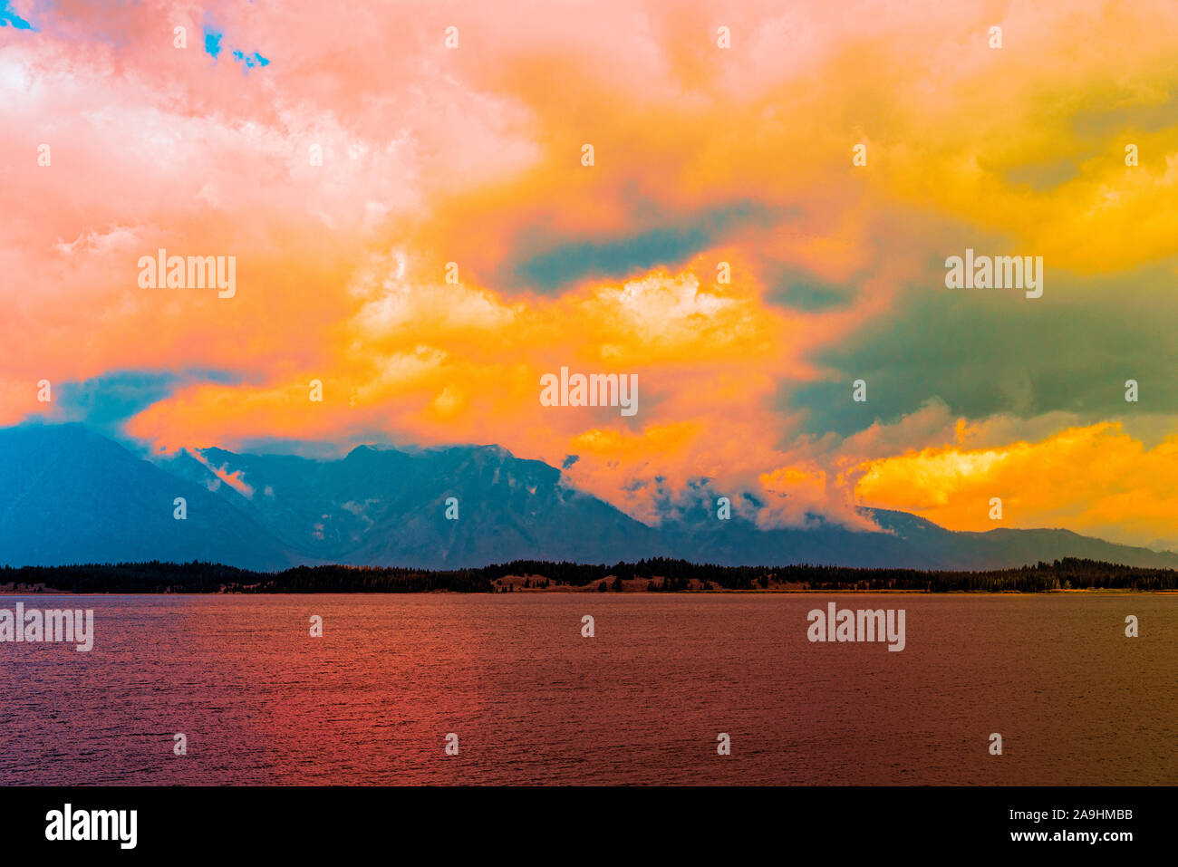 Lake with Teton mountain beyond covered in clouds at sunset with colorful sky. Stock Photo