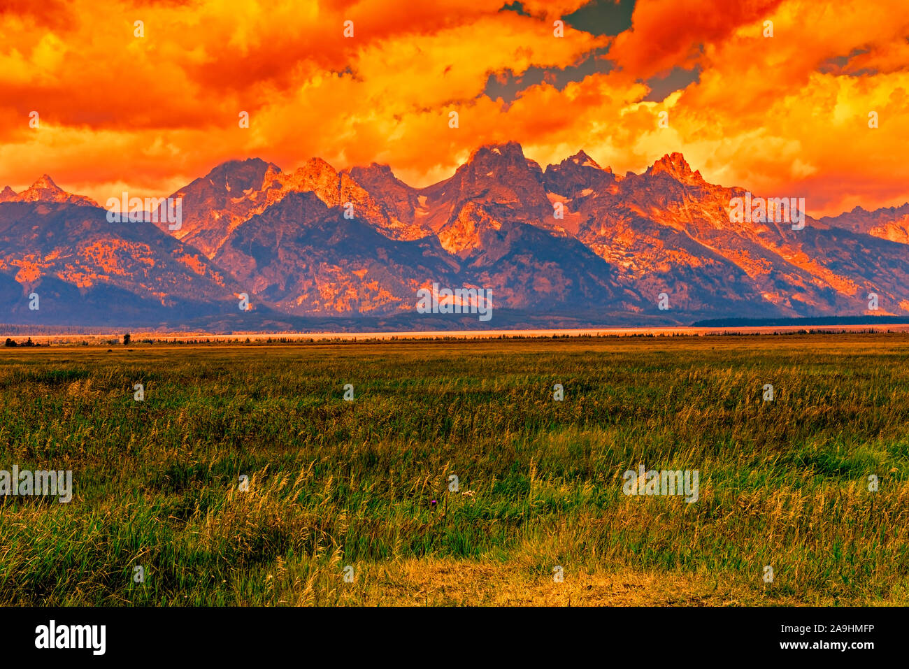 Sunset over Grand Teton National Park, tall Rocky Mountains, green grassy fields under a colorful cloudy sky. Stock Photo